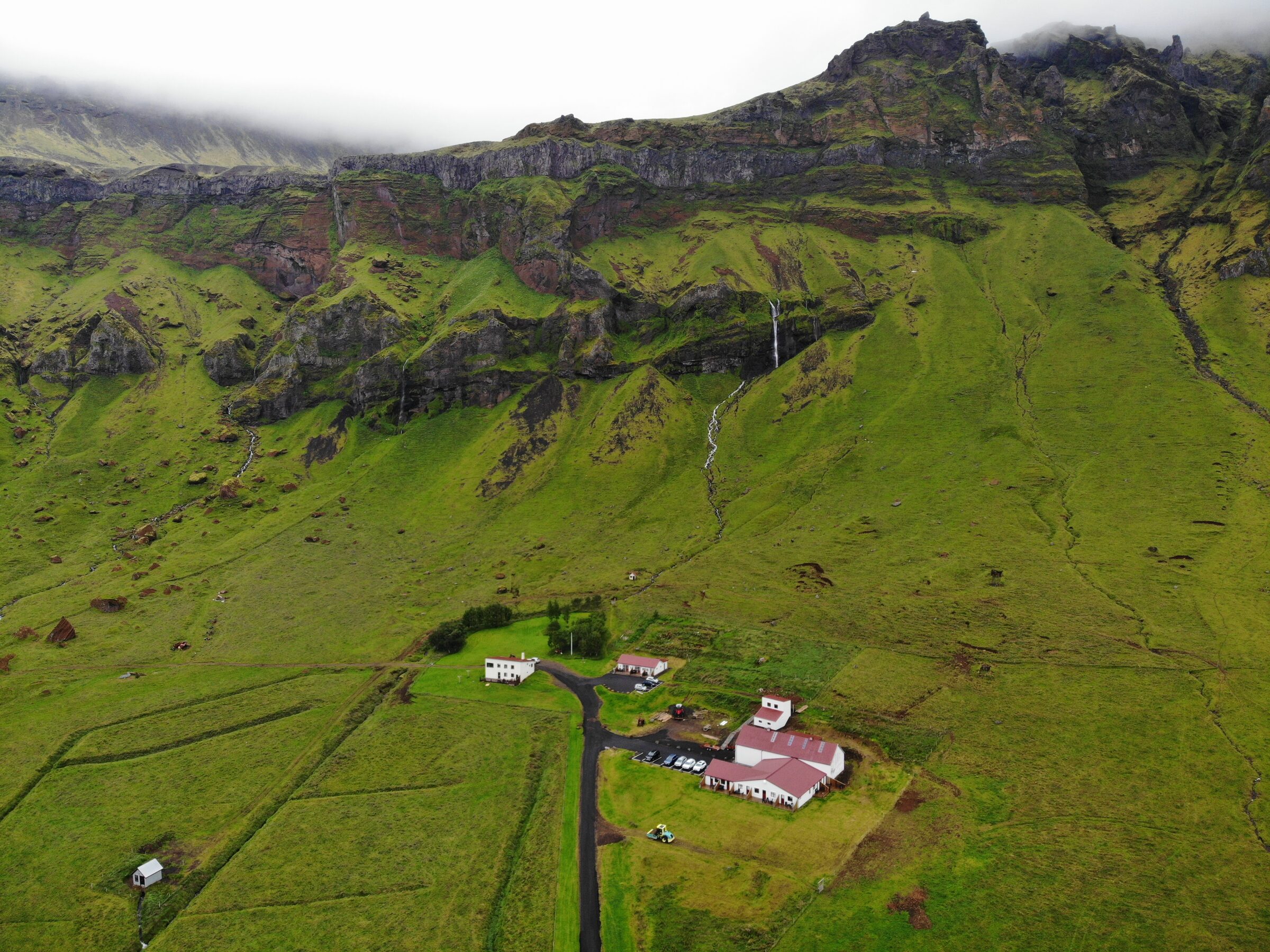 The farm at Varmahlíð from the air, on the green strip between the cliffs and the sea